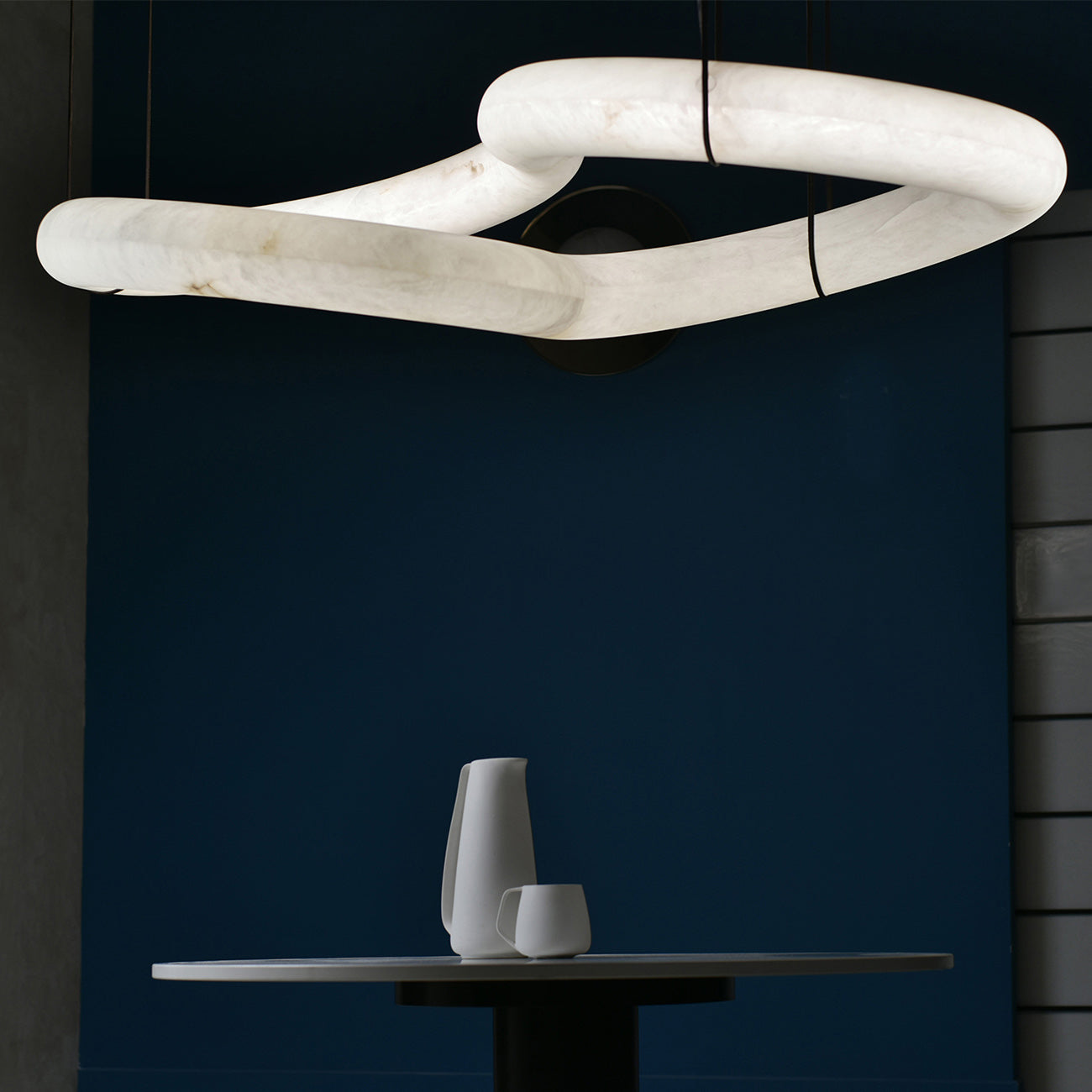 Close-up of the Clérachic alabaster ring chandelier's linked stone loops against a deep navy wall above a round table.