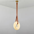 The Clérachic Alabaster Ring Pendant Light seen full length, tan leather doubled through the glowing stone hoop below a brass canopy.