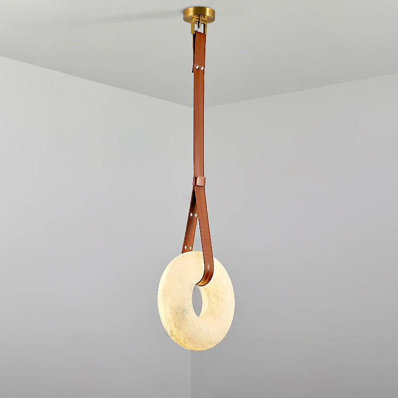 The Clérachic Alabaster Ring Pendant Light seen full length, tan leather doubled through the glowing stone hoop below a brass canopy.