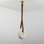 Clérachic Alabaster Ring Pendant Light hung high in a white room corner, the brown strap doubling into a loop through the ring.