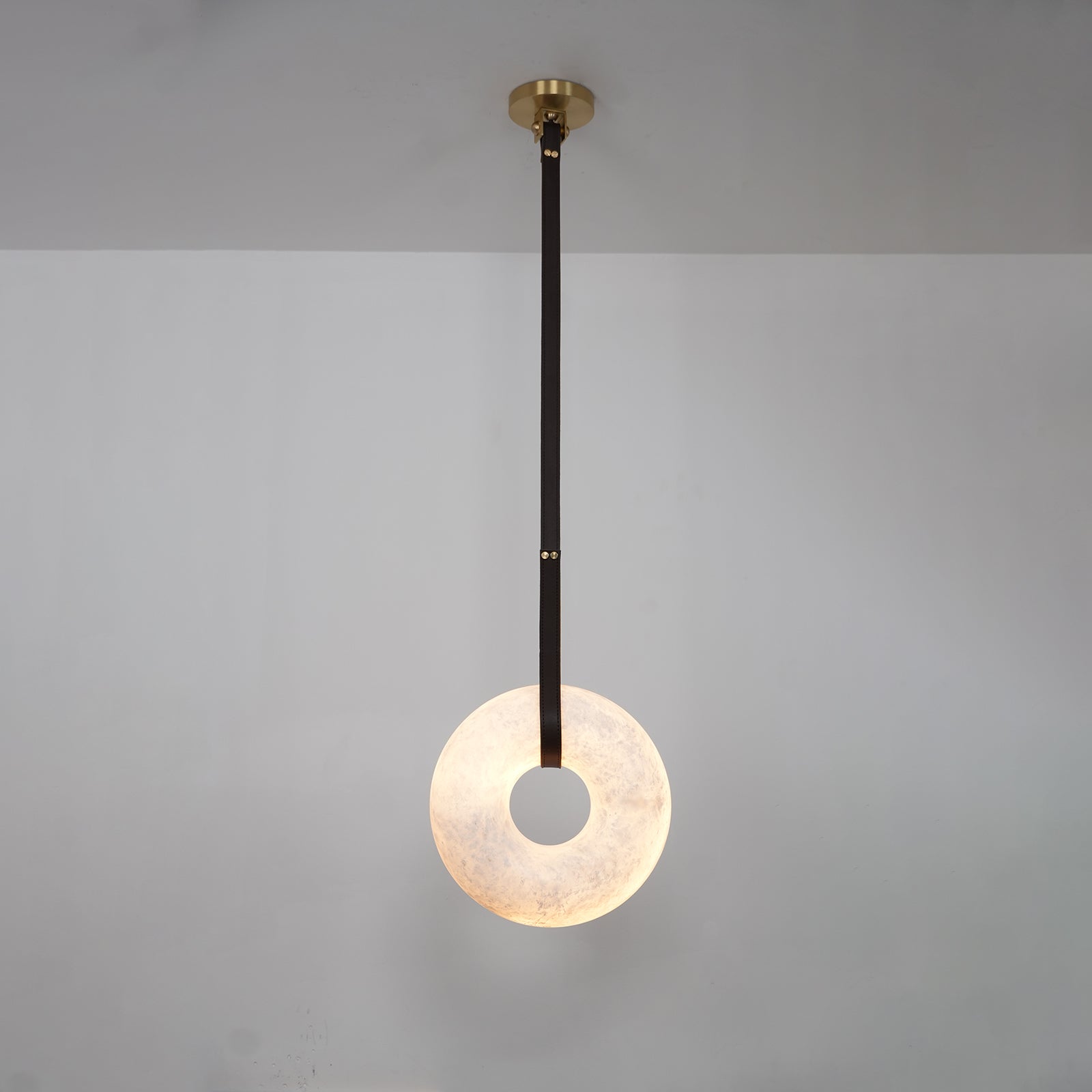 A single dark strap drops the Clérachic Alabaster Ring Pendant Light down a grey wall, the ring lit from within.