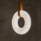 Close view of the Clérachic Alabaster Ring Pendant Light against dark plaster, tan straps looped through the glowing veined stone.