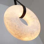 Angled close-up of the Clérachic Alabaster Ring Pendant Light from below, warm light showing the alabaster grain around the strap.