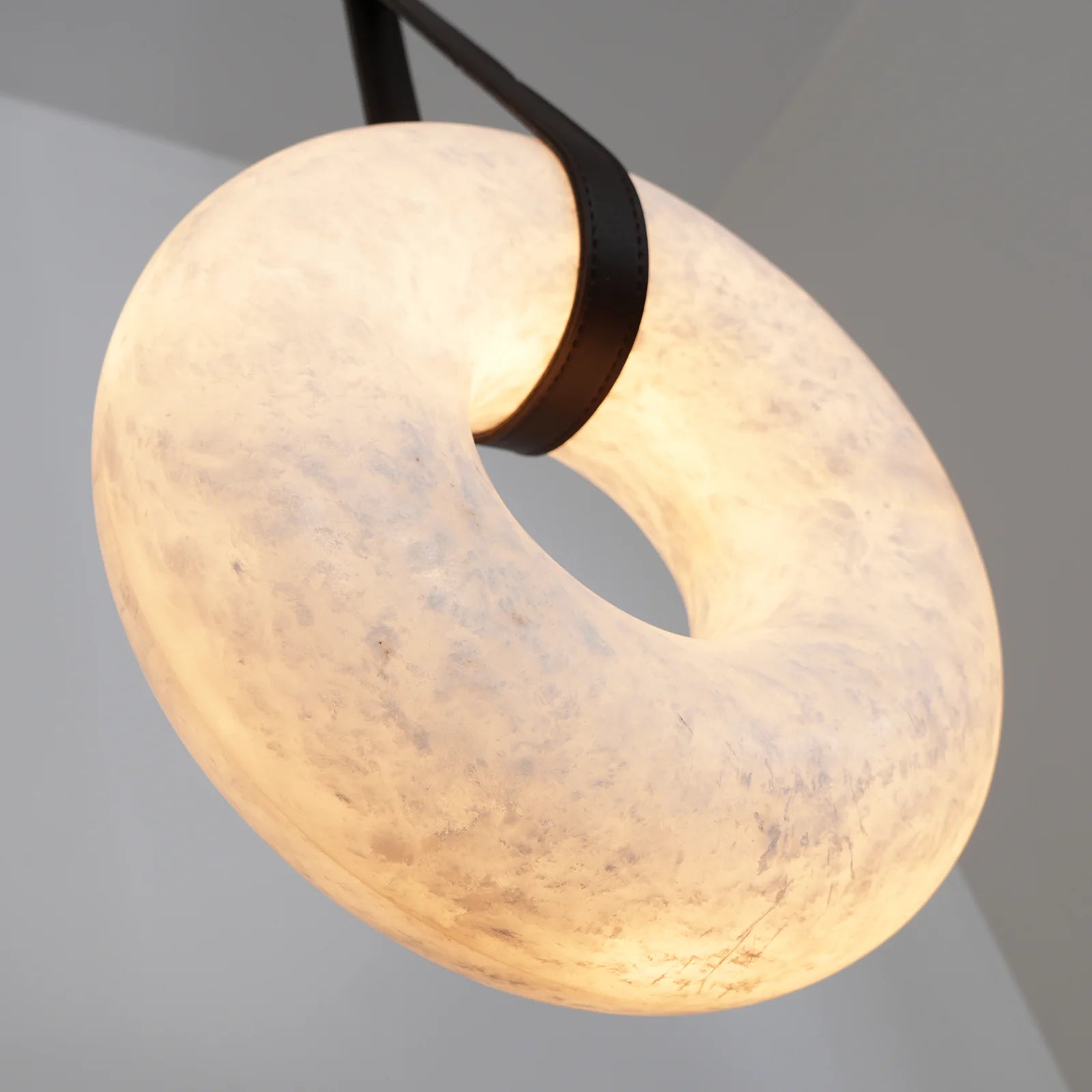Angled close-up of the Clérachic Alabaster Ring Pendant Light from below, warm light showing the alabaster grain around the strap.