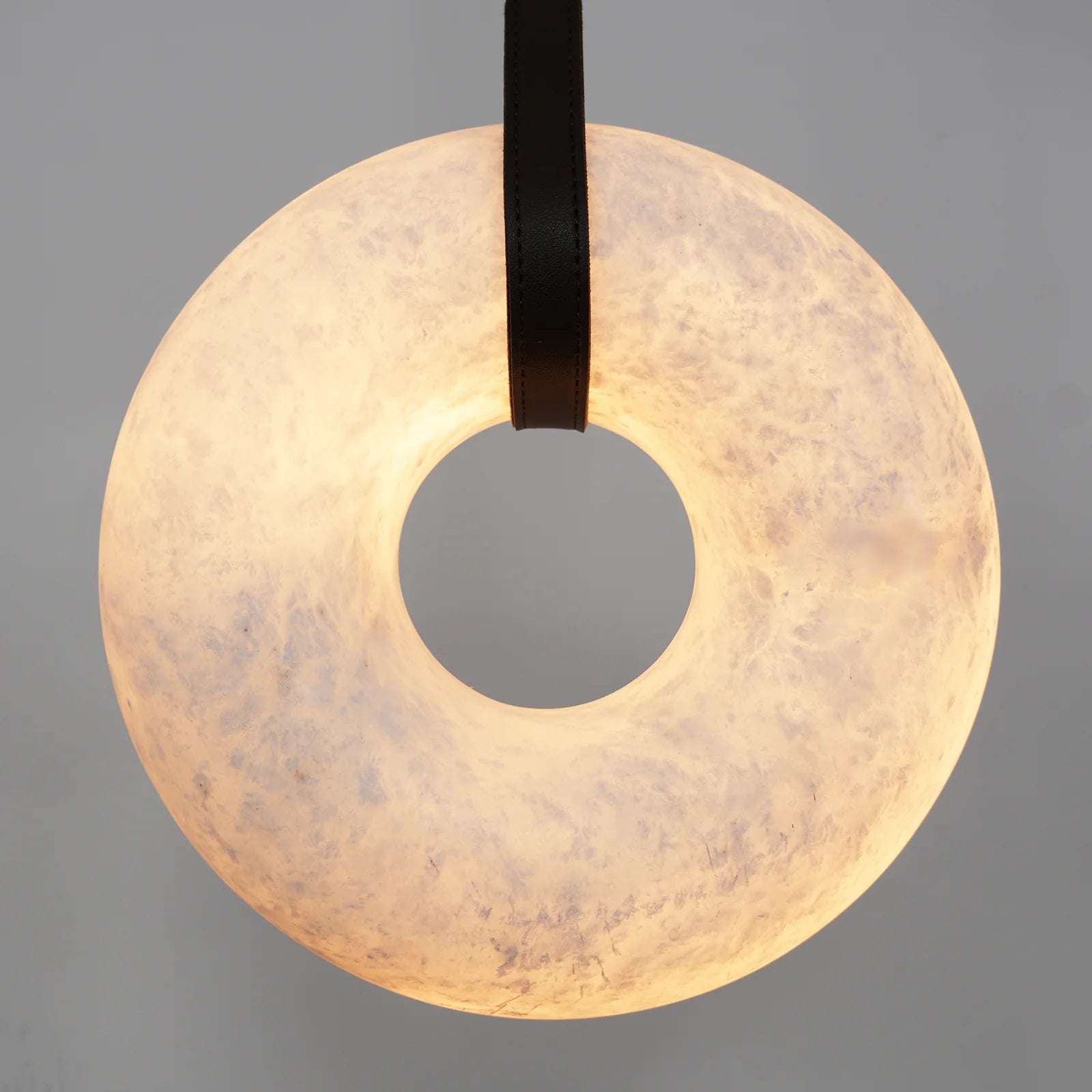 Tight frame on the Clérachic Alabaster Ring Pendant Light, the black strap passing through a wide, softly lit alabaster ring.