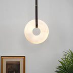 The Clérachic Alabaster Ring Pendant Light glowing beside a gilt-framed print, hung close to the wall on a slim dark strap.
