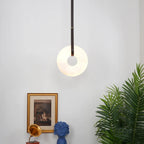 Wide view of a room corner with the Clérachic Alabaster Ring Pendant Light lit above a gilt print and a blue ceramic bust.