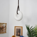 Switched off, the Clérachic Alabaster Ring Pendant Light hangs as plain white stone on a looped strap between two framed prints.