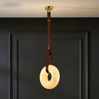 Clérachic Alabaster Ring Pendant Light glowing warm against a dark panelled wall, brown strap running up to the brass canopy.