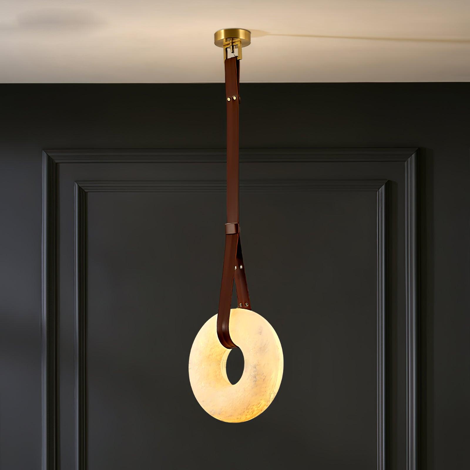 Clérachic Alabaster Ring Pendant Light glowing warm against a dark panelled wall, brown strap running up to the brass canopy.