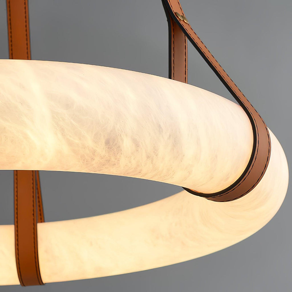 Lit close-up of the Clérachic Alabaster Ring Pendant Light, a leather strap curving under the glowing band of veined stone.