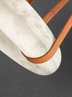 Graphic close-up of the Clérachic Alabaster Ring Pendant Light, a tan leather strap looping under the white stone against dark grey.