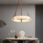Clérachic Alabaster Ring Pendant Light lit above a round dining table, its warm halo reaching the vase and figures set below.