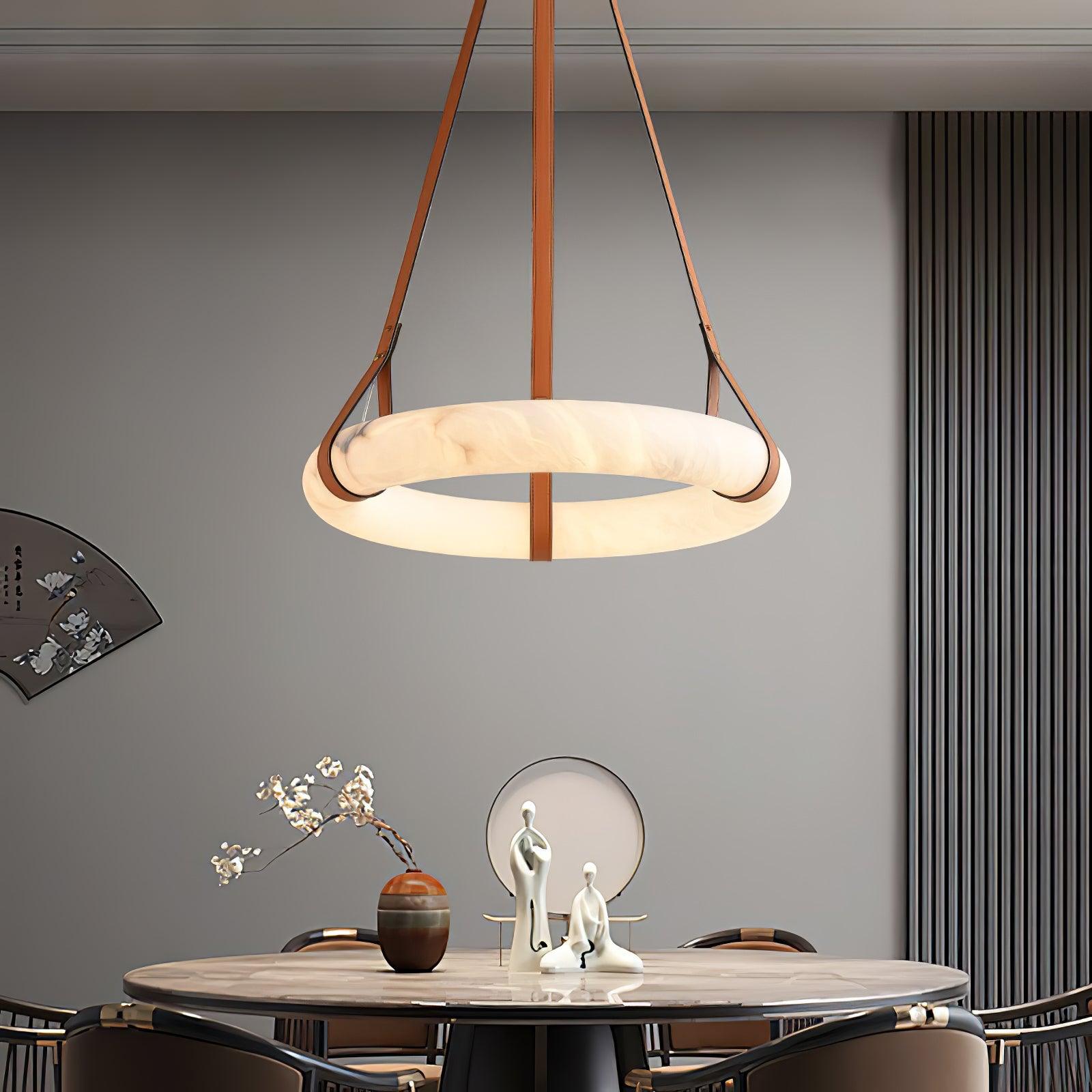 Clérachic Alabaster Ring Pendant Light lit above a round dining table, its warm halo reaching the vase and figures set below.