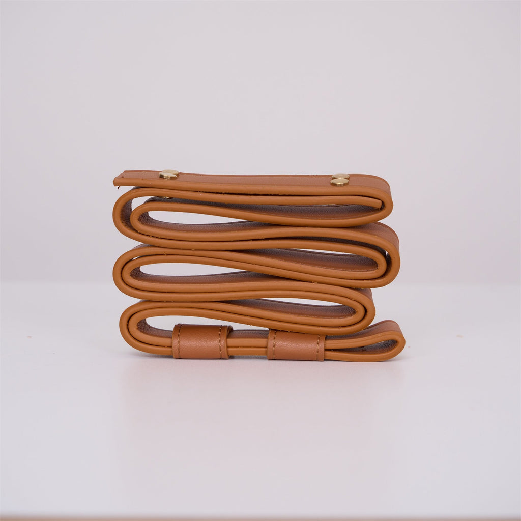 Tan leather strap for the Clérachic Alabaster Ring Pendant Light coiled edge-on, its rolled edge and brass rivets in view.