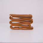 Tan leather strap for the Clérachic Alabaster Ring Pendant Light coiled edge-on, its rolled edge and brass rivets in view.