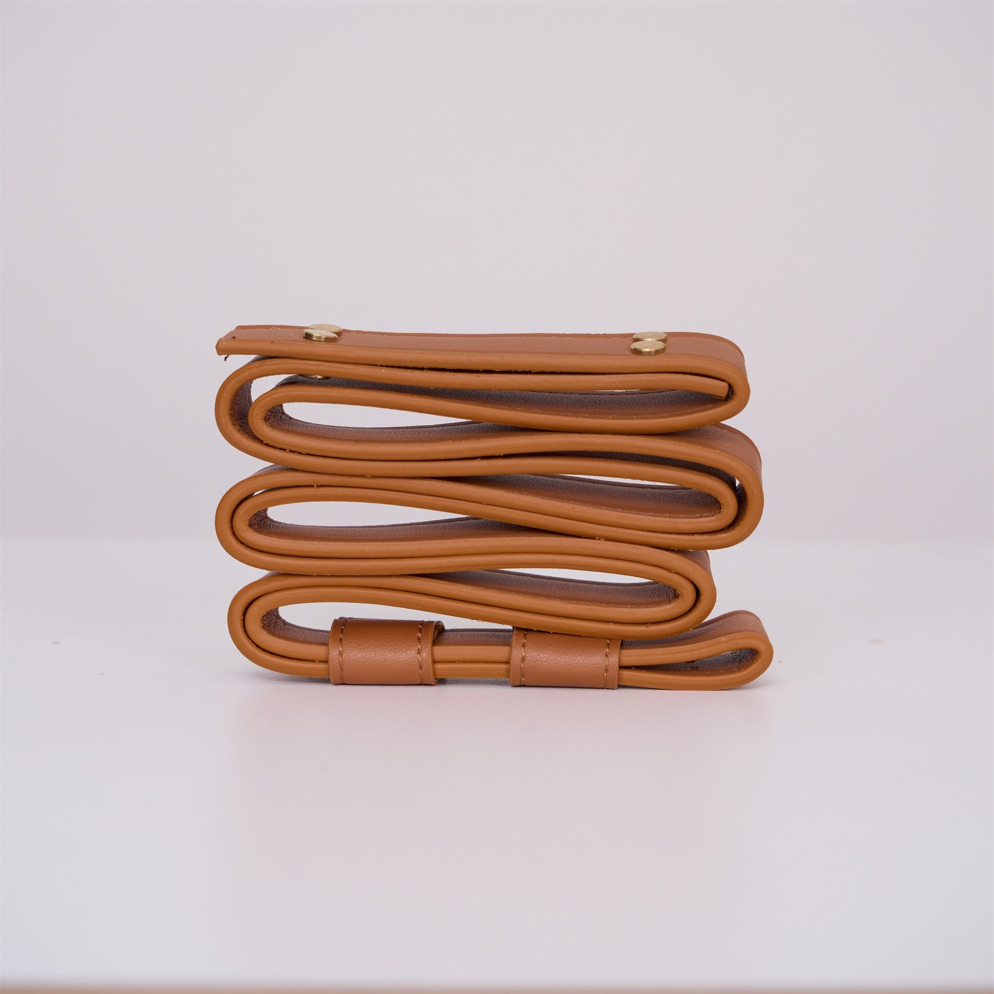Tan leather strap for the Clérachic Alabaster Ring Pendant Light coiled edge-on, its rolled edge and brass rivets in view.