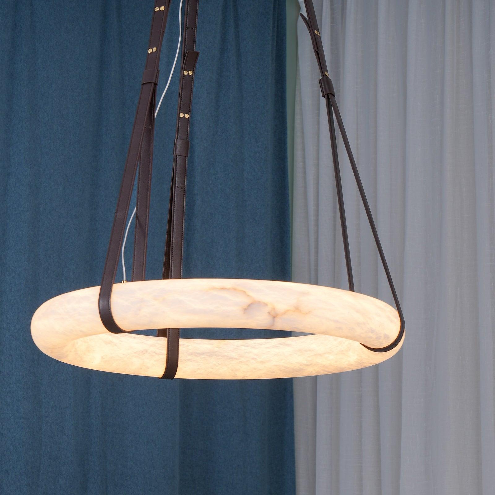Clérachic Alabaster Ring Pendant Light lit against blue and white curtains, the stone band glowing evenly all the way round.