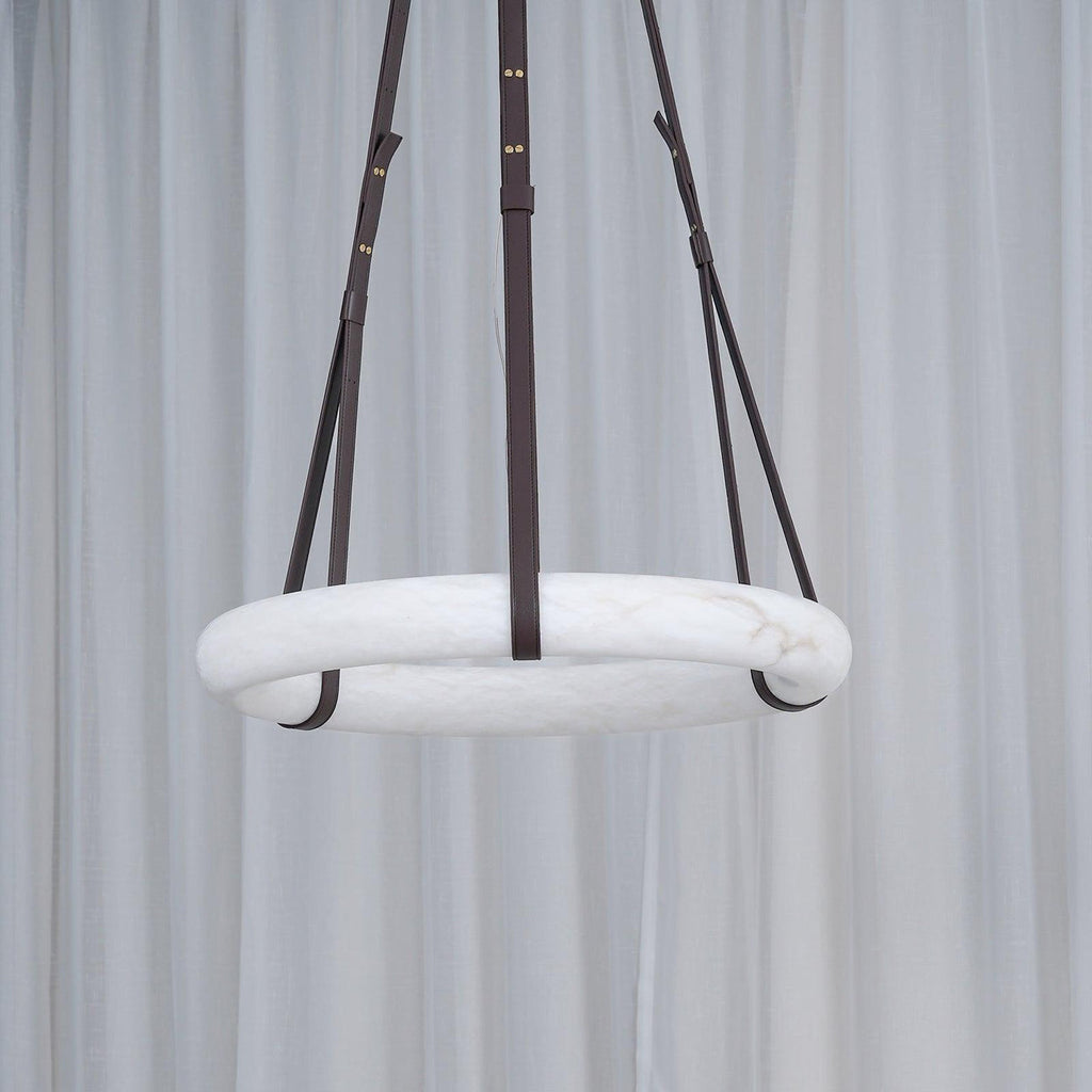 The Clérachic Alabaster Ring Pendant Light unlit in front of a sheer white curtain, reading as a pale stone hoop on dark straps.
