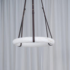 The Clérachic Alabaster Ring Pendant Light unlit in front of a sheer white curtain, reading as a pale stone hoop on dark straps.