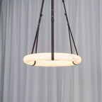 Clérachic Alabaster Ring Pendant Light switched on before a sheer white curtain, the whole band turning warm from the inside.