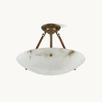 A Clérachic semi-flush ceiling light with a veined alabaster bowl and three antique brass arms, on a plain off-white backdrop.