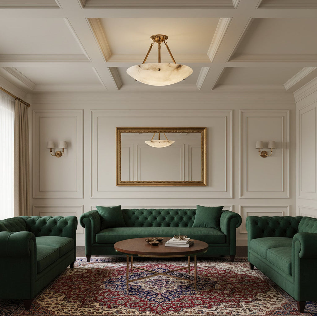 A Clérachic alabaster ceiling light lit above a living room with green tufted sofas and a patterned rug.