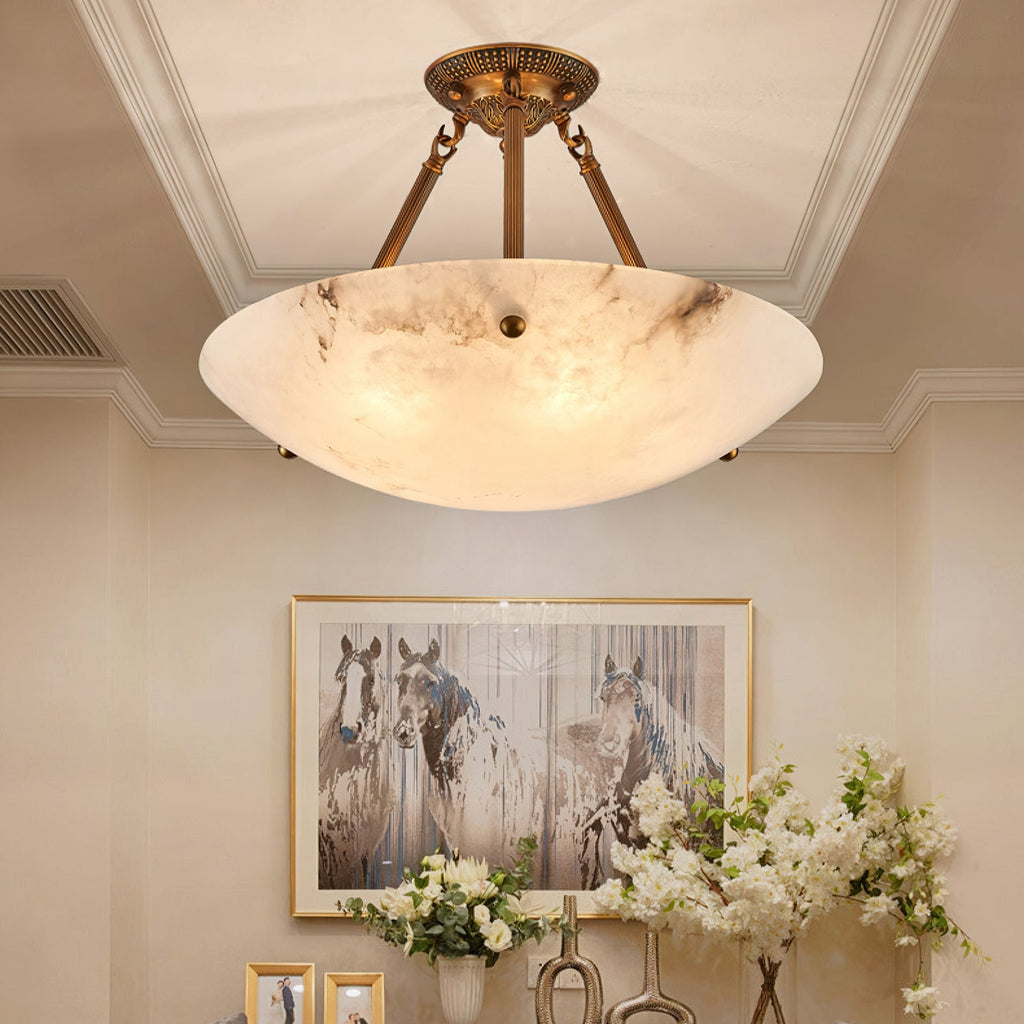 A large Clérachic alabaster bowl light with dark veining hangs in a hall, with a framed horse print and white flowers below.