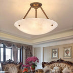 An antique brass and alabaster Clérachic ceiling light above a sitting room with carved sofas and a bunch of pink orchids.