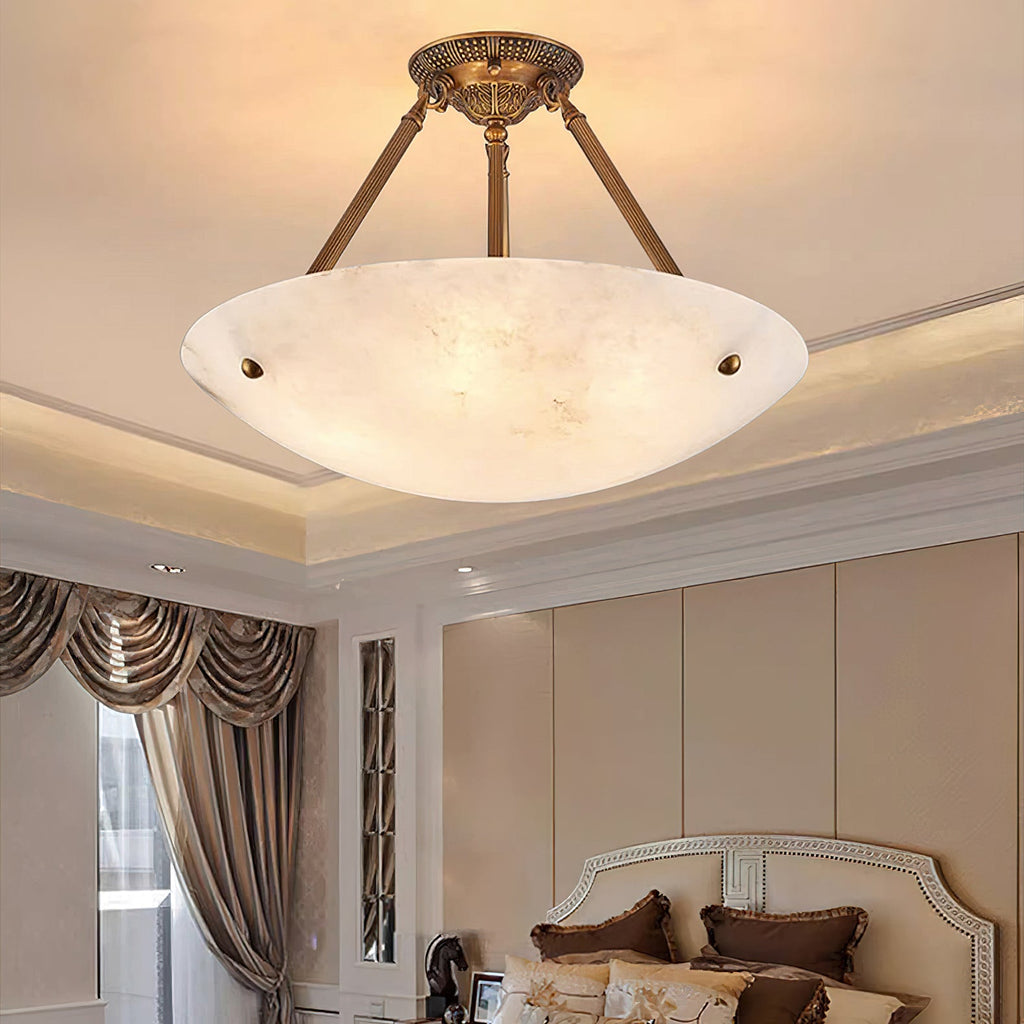A Clérachic alabaster ceiling light lit above a bedroom with a cream headboard and heavy draped curtains.