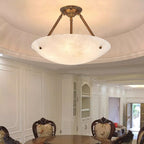 This Clérachic alabaster semi-flush light hangs in a round ceiling recess above a dining room with carved chairs.