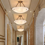 Three Clérachic alabaster bowl lights line a long panelled hallway, each hung from antique brass arms.