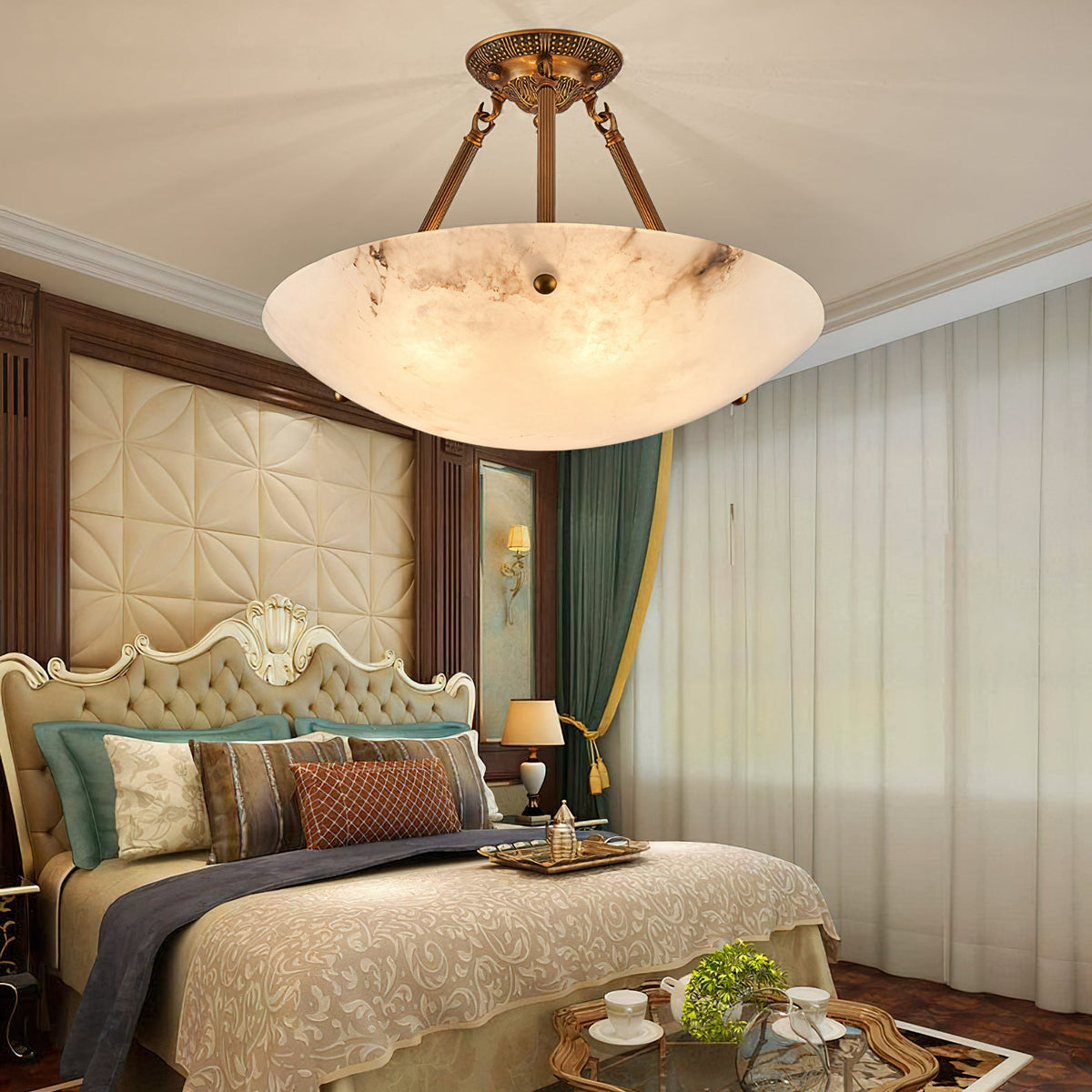 The Clérachic alabaster bowl light glows over a bedroom with a gold-framed bed, a green curtain and a tray with a teacup.