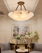 A veined alabaster bowl on antique brass arms, this Clérachic ceiling light hangs above a console with white flowers and a horse print.