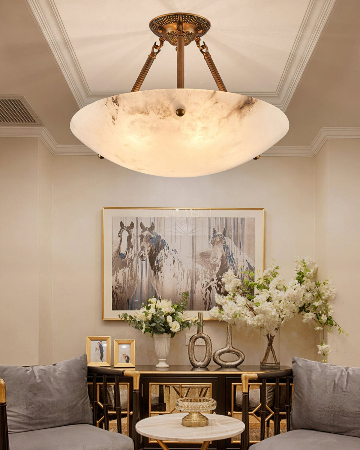 A veined alabaster bowl on antique brass arms, this Clérachic ceiling light hangs above a console with white flowers and a horse print.