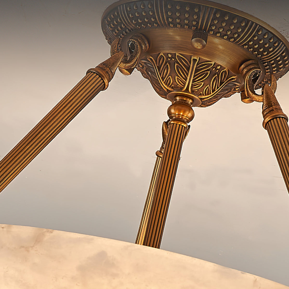 Looking up at the three ribbed antique brass arms and the patterned canopy of this Clérachic alabaster ceiling light.