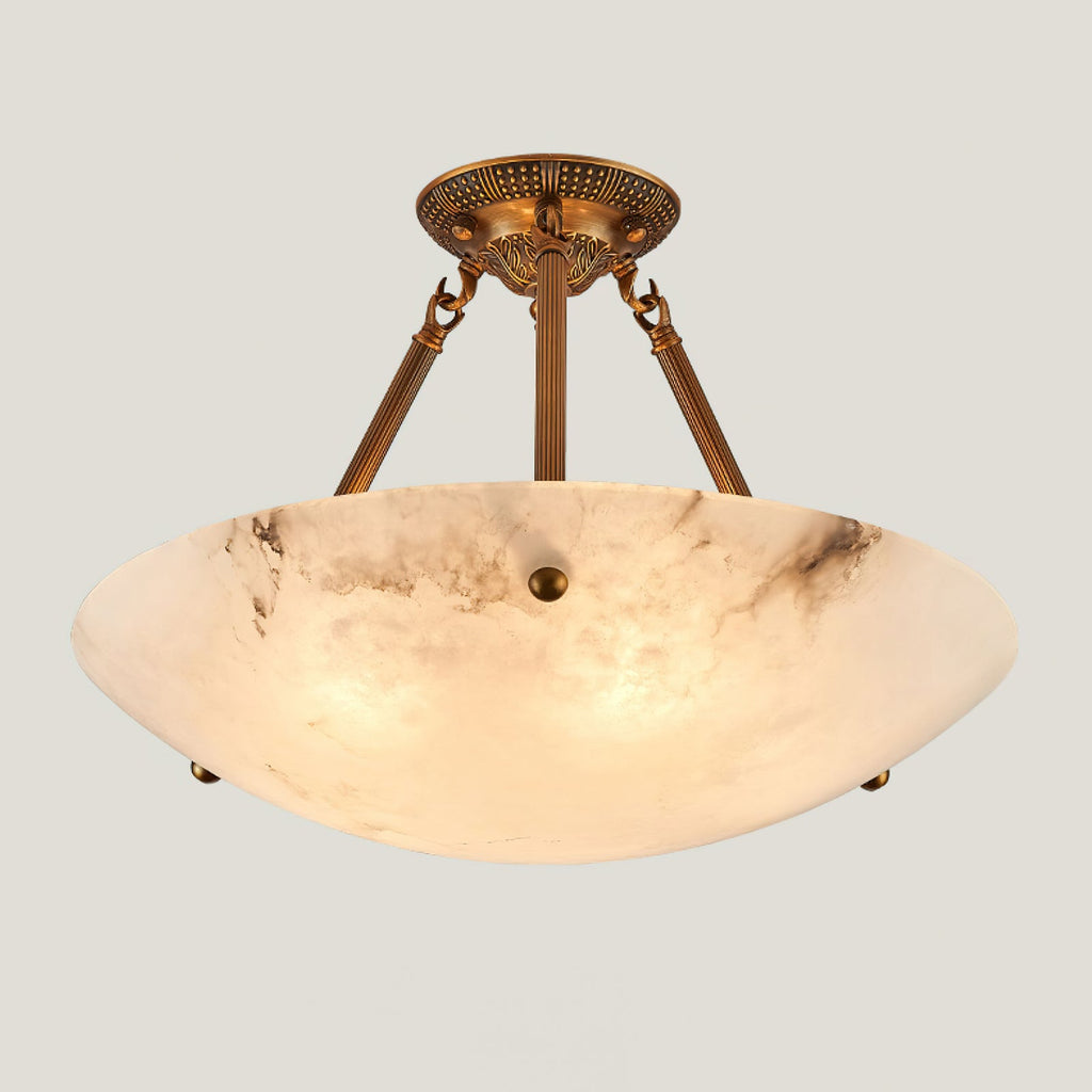 A lit Clérachic alabaster bowl light with antique brass arms and canopy, glowing amber against a pale backdrop.