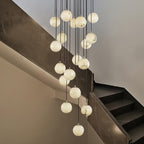 Clérachic alabaster spheres drop at different heights past a dark marble stair wall, each glowing a soft white.