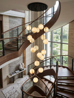 This Clérachic cluster of glowing alabaster spheres hangs from a black canopy down a curved walnut staircase beside a tall garden window.