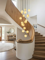 Warm-glowing Clérachic alabaster spheres hang beside a pale oak spiral stair with a curved white wall, above a round rug.