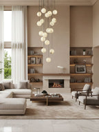 Clérachic alabaster spheres hang in a tall living room, above a cream sectional sofa, a low table and a fireplace with shelving.