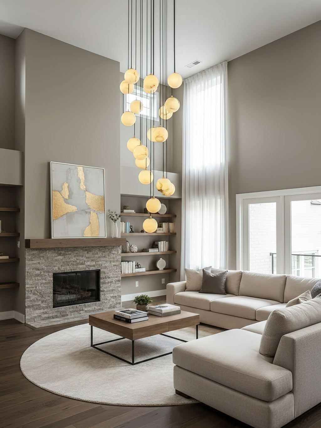 A Clérachic cluster of alabaster spheres hangs high in a double-height lounge with a stone fireplace, a cream sectional and a round rug.