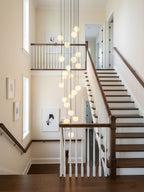 Clérachic alabaster spheres run down a traditional stairwell with white balusters and a dark wood handrail, seen from the landing.