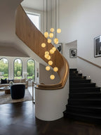 Clérachic alabaster spheres glow beside a curved oak balustrade, with black stairs and arched windows in the room beyond.