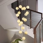 Close view of the Clérachic alabaster spheres lit warm, hanging beside a walnut stair rail with mesh panels and a small bonsai below.