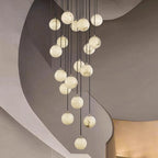 Clérachic alabaster spheres, lit soft white, hang in front of the sweeping curves of a plaster stairwell.