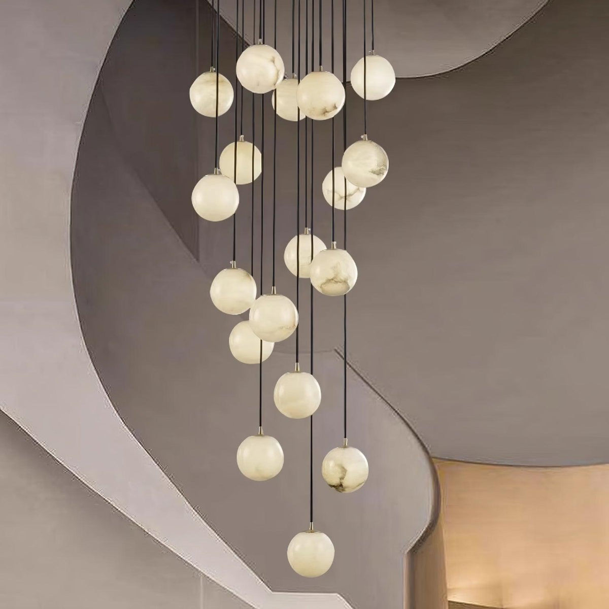 Clérachic alabaster spheres, lit soft white, hang in front of the sweeping curves of a plaster stairwell.