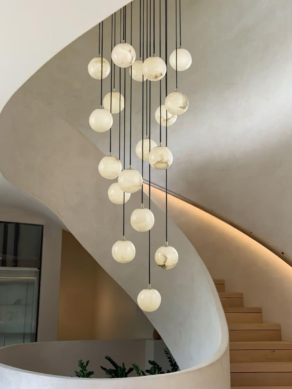 Clérachic alabaster spheres hang inside a curved plaster stair, with a glowing light line along the wall and a few green leaves below.