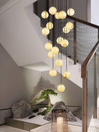 Clérachic alabaster spheres descend past a walnut rail with mesh panels, above a small rock and bonsai garden at the foot of the stair.