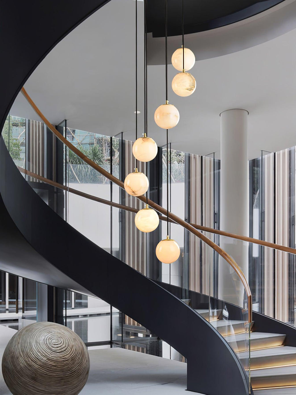 A short run of Clérachic alabaster spheres hangs in front of a black spiral staircase in a glass-walled atrium.